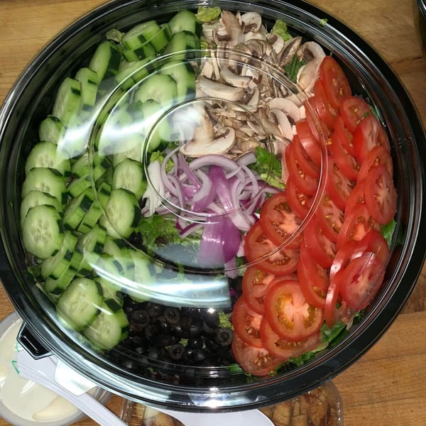 A large Homerun Pizza salad with cucumbers, mushrooms, red onions, tomatoes, and black olives.
