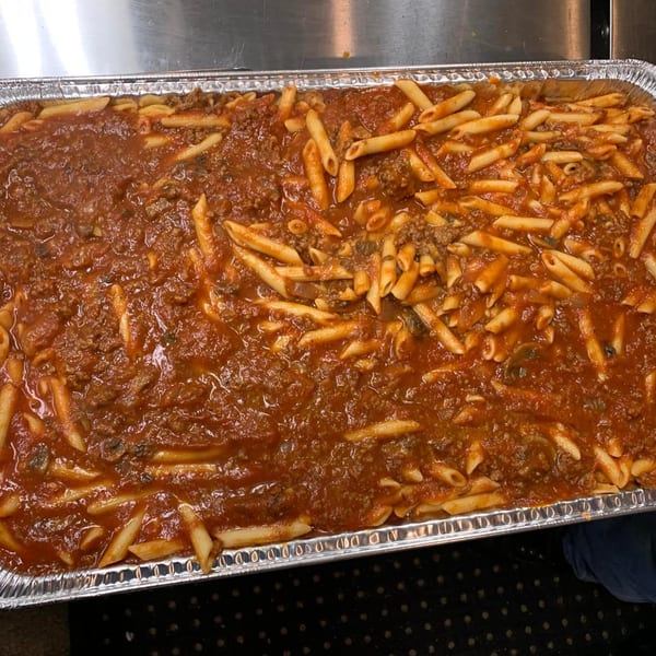 A large aluminum tray filled with penne pasta and a rich, meaty red sauce.