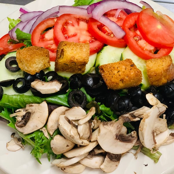 A fresh garden salad with lettuce, tomatoes, red onions, cucumbers, black olives, mushrooms, and croutons.