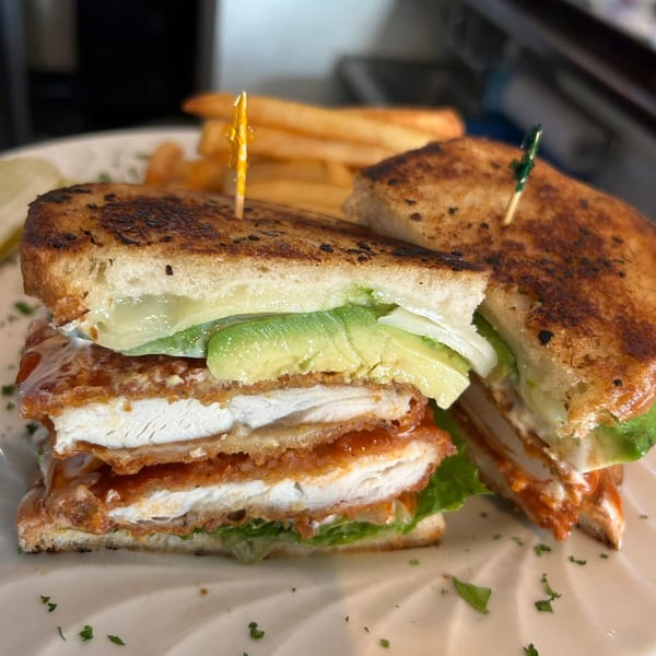 A crispy chicken sandwich with avocado, lettuce, and sauce, served with fries on a white plate.