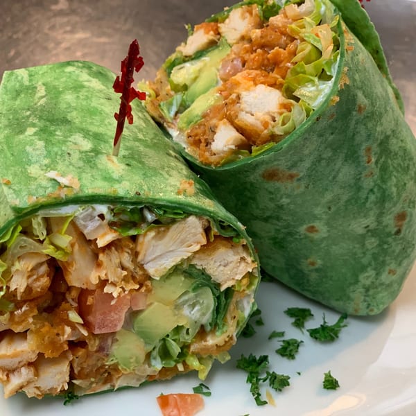 Two halves of a green tortilla wrap filled with chicken, lettuce, avocado, and tomatoes.