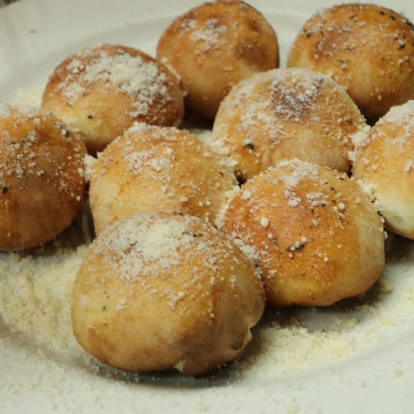 Close-up of golden-brown garlic knots, sprinkled with Parmesan cheese, on a white plate.