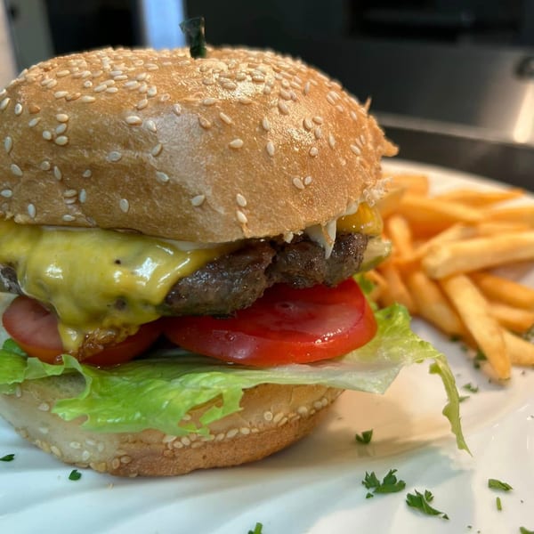 Cheeseburger with lettuce, tomato, and a side of golden french fries on a white plate.