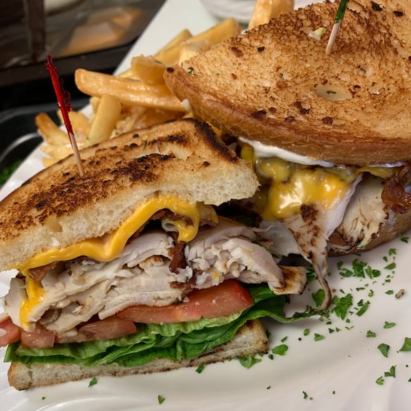A grilled turkey and cheese sandwich with lettuce, tomato, and bacon, served with french fries.