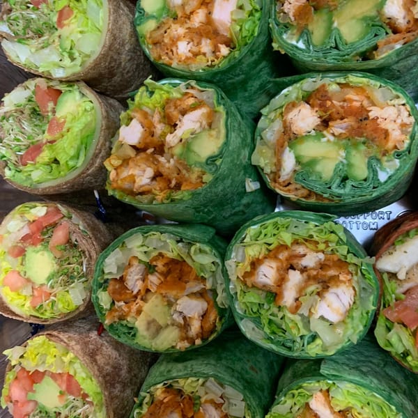 Close-up of several wraps, some with green tortillas and chicken, others with brown tortillas and vegetables.